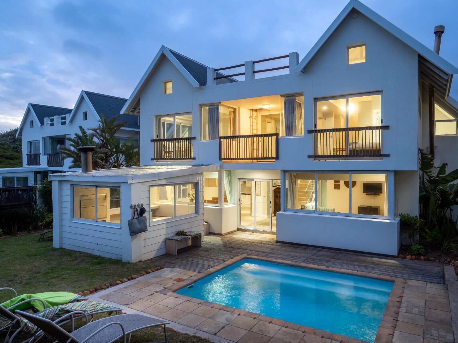 Una casa moderna de dos pisos con piscina, ventanas amplias y un balcón.