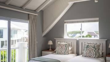 A bedroom with a sloped ceiling, a large bed with two pillows, a bedside table with a lamp, and a window with a view of buildings.