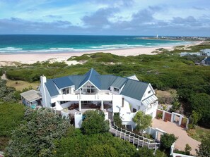A large, modern house with a spacious deck and multiple windows, overlooking a beach and ocean. - Beach Break Guest Houses and Villas (Cape Saint Francis)