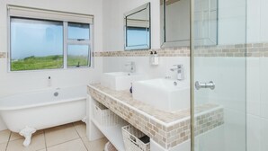 Un baño moderno con bañera, dos lavamanos, cabina de ducha de vidrio y un ventanal con vistas.