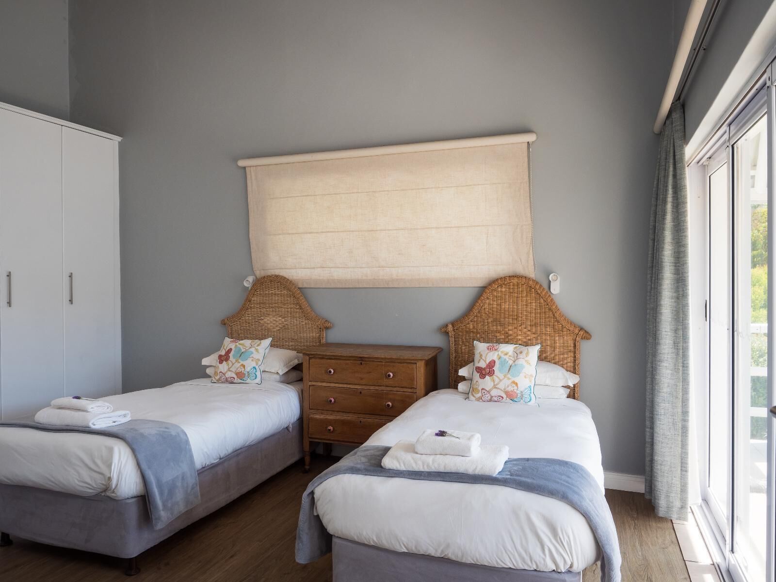 Un dormitorio con dos camas, un aparador de madera y un ventanal grande.
