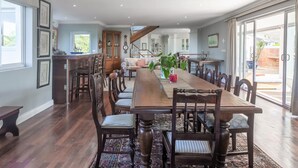 Un vaste espace dédié à la salle à manger, avec une longue table en bois entourée de chaises, une cuisine en arrière-plan et un escalier menant à un niveau supérieur.