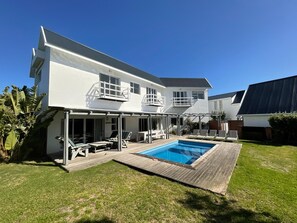 Ein zweistöckiges Haus mit Swimmingpool, einer überdachten Terrasse mit Liegestühlen und einem gepflegten Rasen.