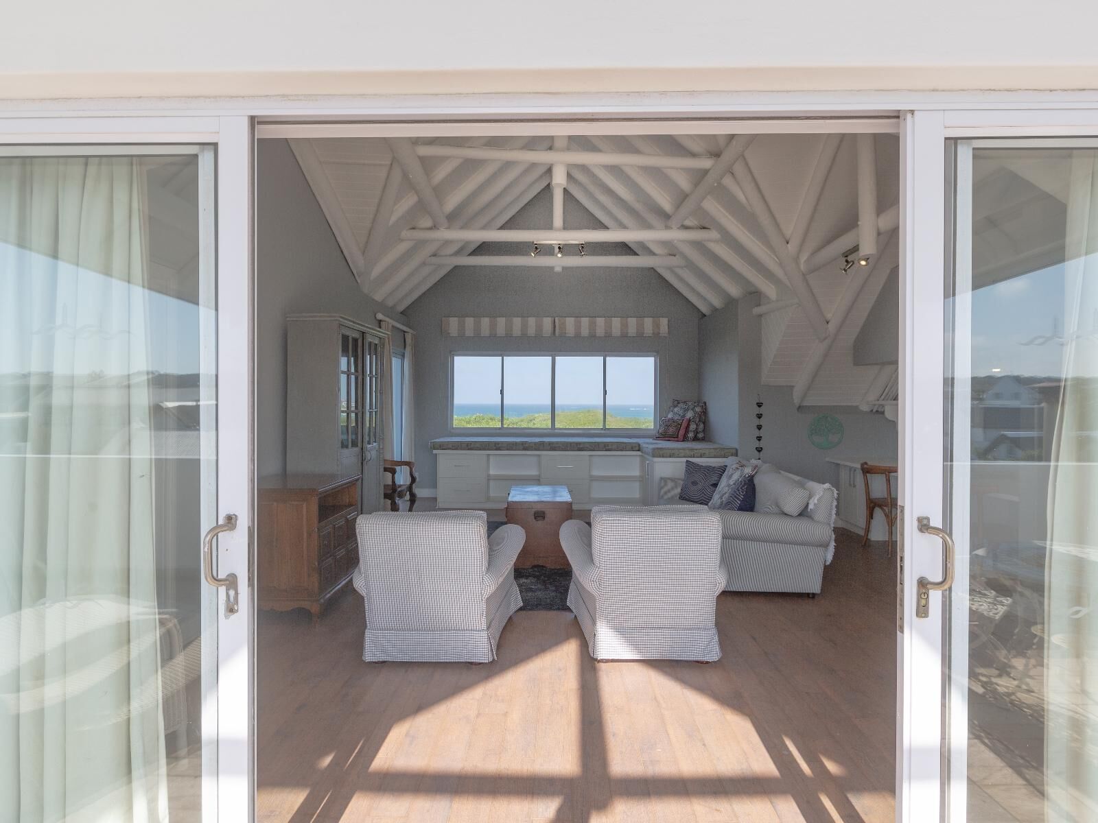 Una habitación espaciosa con un ventanal grande que ofrece vistas panorámicas, una zona de estar acogedora con dos sillones y un sofá, y suelo de madera.