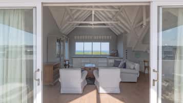 Una habitación espaciosa con un ventanal grande que ofrece vistas panorámicas, una zona de estar acogedora con dos sillones y un sofá, y suelo de madera.