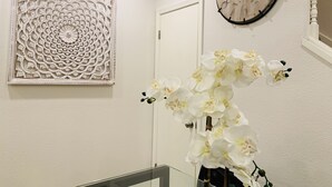 Una habitación con un panel decorativo, un reloj y un florero con flores blancas.