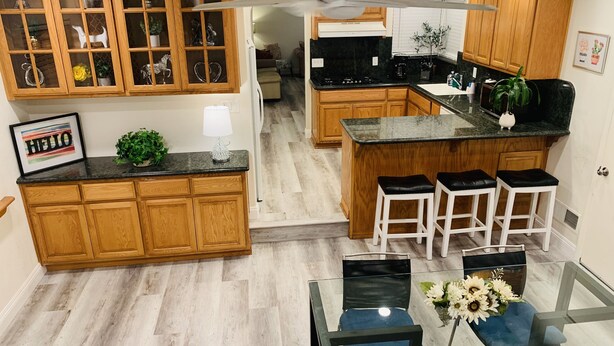 Una cocina moderna con armarios de madera, una isla central con taburetes y una mesa de comedor de vidrio con sillas azules.