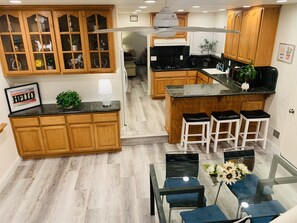A modern kitchen with wooden cabinets, a central island with stools, and a glass dining table with blue chairs. - Charming House in San Jose Evergreen 5Br/3Bt 8Beds (San Jose)