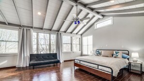 A spacious bedroom with a large bed, a dark leather sofa, and a ceiling fan.