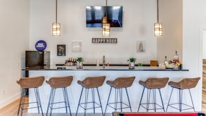 A bar area with six wicker stools, a flat-screen TV mounted above the bar, and a 'Happy Hour' sign.