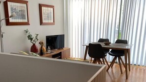 Un salon moderne avec un coin repas, comprenant un téléviseur à écran plat, une table à manger en bois avec des chaises, et deux tableaux encadrés accrochés au mur.