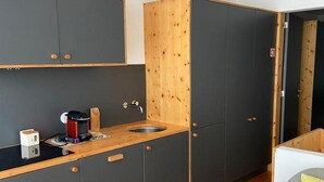 Une cuisine de taille réduite, avec des meubles de couleur sombre, un mur d’accent en bois et un évier.