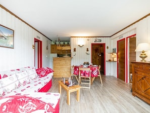 Ein gemütliches Wohnzimmer mit einer Couch, einem Esstisch mit Stühlen, einem Holzschrank und einer Küchenzeile mit Schränken und einer Pendelleuchte.