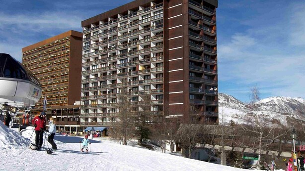 A multi-story hotel with a modern architectural design, featuring balconies and a ski slope in the background. - Nice apartment for 4 people with WIFI, pool, TV and pets allowed (Le Corbier)