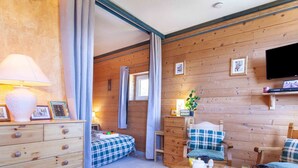 A cozy room with wooden walls, a bed with a plaid bedspread, a wooden dresser, a coffee table with breakfast items, and a television mounted on the wall. - Nice apartment for 4 people with WIFI, pool, TV and pets allowed (Le Corbier)