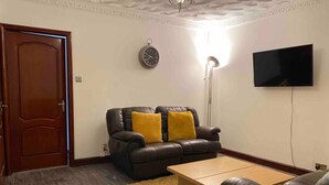 A living room with a dark leather sofa, a wooden coffee table, a yellow rug, a wall-mounted TV, and a door with a light strip. - Cozy Swansea Apartment with 2 Bedrooms (Swansea)