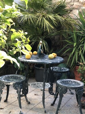 A round metal table with four chairs, surrounded by potted plants and a stone wall. - House Sleeps 4 with Private Garden (Mexilhoeira Grande)