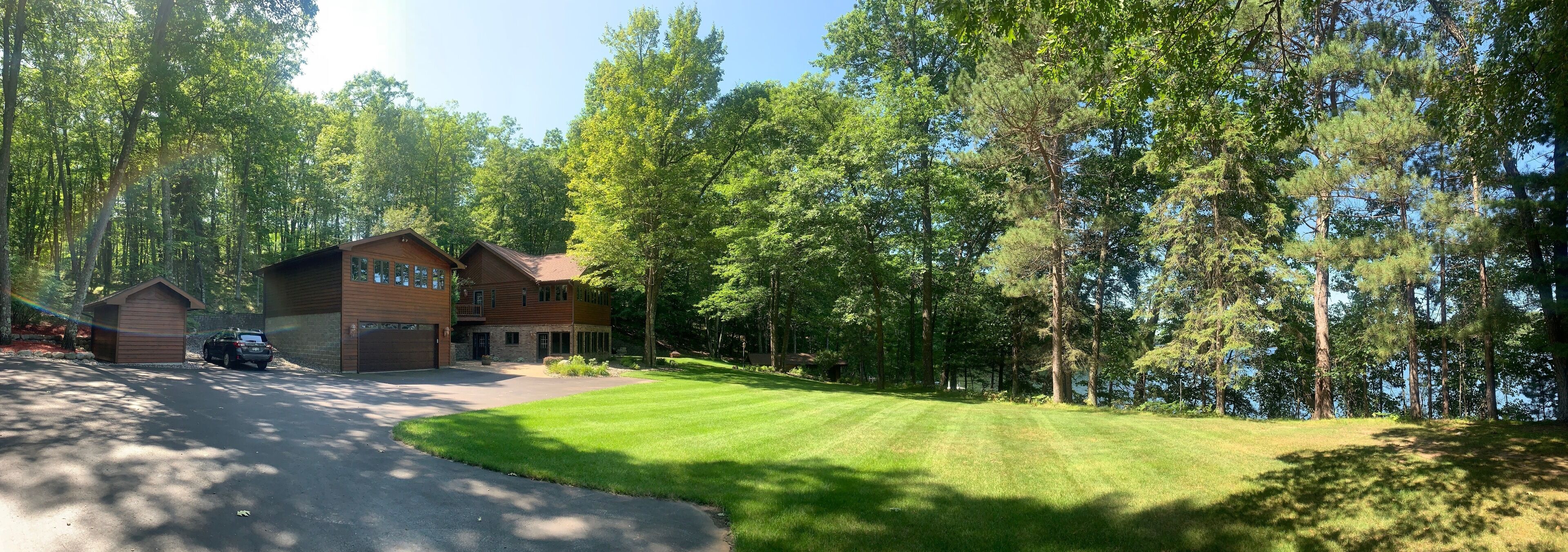 Une cabane à deux étages avec un garage, entourée d’une pelouse bien entretenue et de grands arbres.