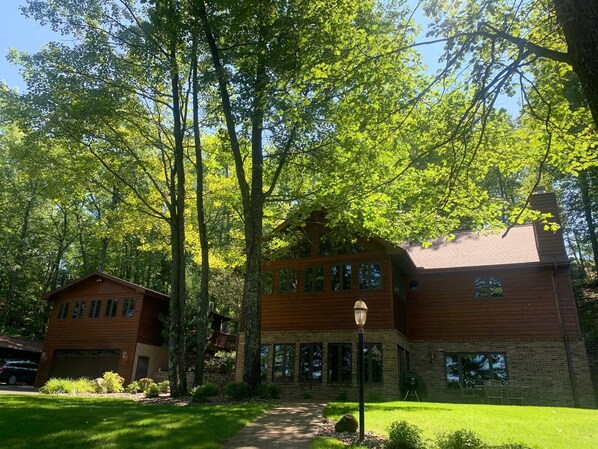 A two-story wooden house with a brick foundation, surrounded by a well-maintained lawn and tall trees.