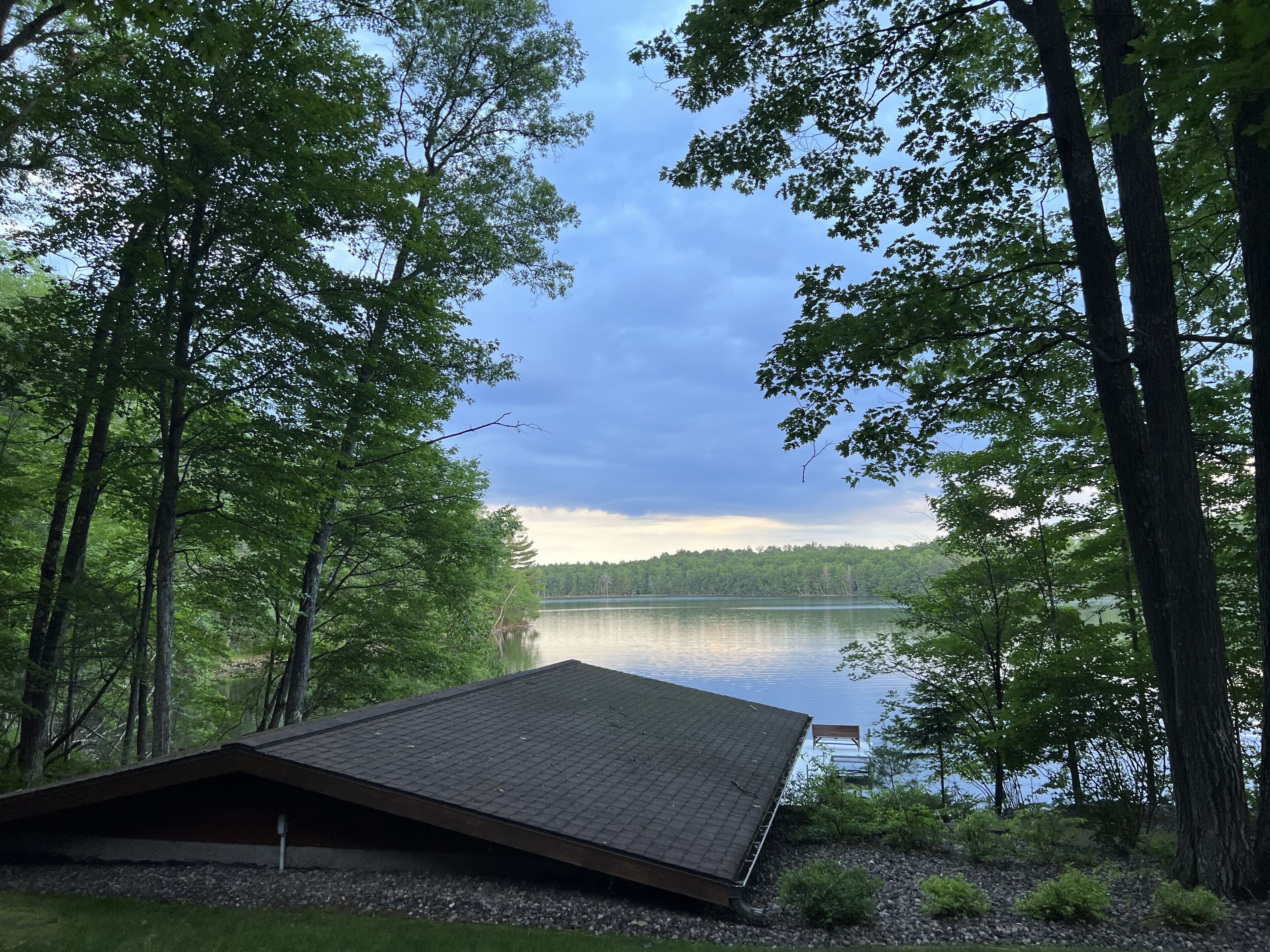 A cabin with a sloped roof overlooking a lake, surrounded by dense trees.