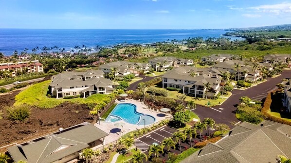 A residential area with a large swimming pool surrounded by houses, a clear view of the ocean, and a well-maintained landscape.