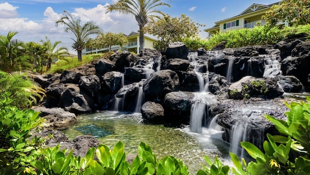 Un complexe hôtelier tropical doté d’une cascade naturelle, d’une végétation luxuriante et d’un bâtiment avec un balcon offrant une vue panoramique.