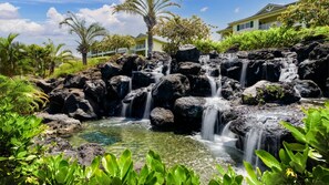A tropical resort with a natural rock waterfall, lush greenery, and a building with a balcony overlooking the scenery.