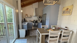 A modern kitchen with a dining area, wooden ceiling, and large windows. - River Rock Beach House, Irish Beach private access (Manchester)