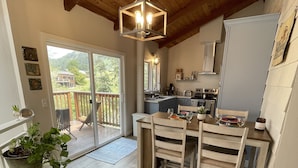 A wooden-floored kitchen with a dining area, a sliding glass door to a balcony, and a hanging light fixture. - River Rock Beach House, Irish Beach private access (Manchester)