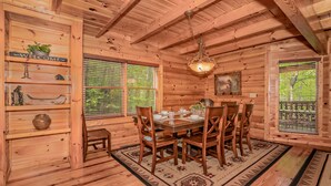 A wooden cabin interior with a dining table set for four, surrounded by wooden chairs. A welcome sign and a shelf with decorative items are visible. - Right on the river! (Sevierville)