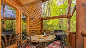 A wooden deck with a round table and chairs, a grill, and a scenic forest view. - Right on the river! (Sevierville)