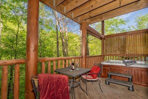 Une terrasse en bois avec une table et des chaises, un jacuzzi et une vue sur une forêt.