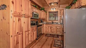 A wooden cabin-style kitchen with built-in appliances, a window with blinds, and a refrigerator. - Right on the river! (Sevierville)
