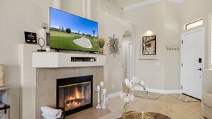 A living room with a fireplace, a television, and a decorative wall piece. - Two King 👑 Suites,🌴Cozy Palm Desert Home Getaway ❤ 2 Great for Extended Stays! (Palm Desert)