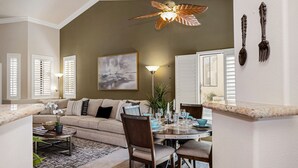A living room with a sofa, dining table, chairs, and a ceiling fan. - Two King 👑 Suites,🌴Cozy Palm Desert Home Getaway ❤ 2 Great for Extended Stays! (Palm Desert)