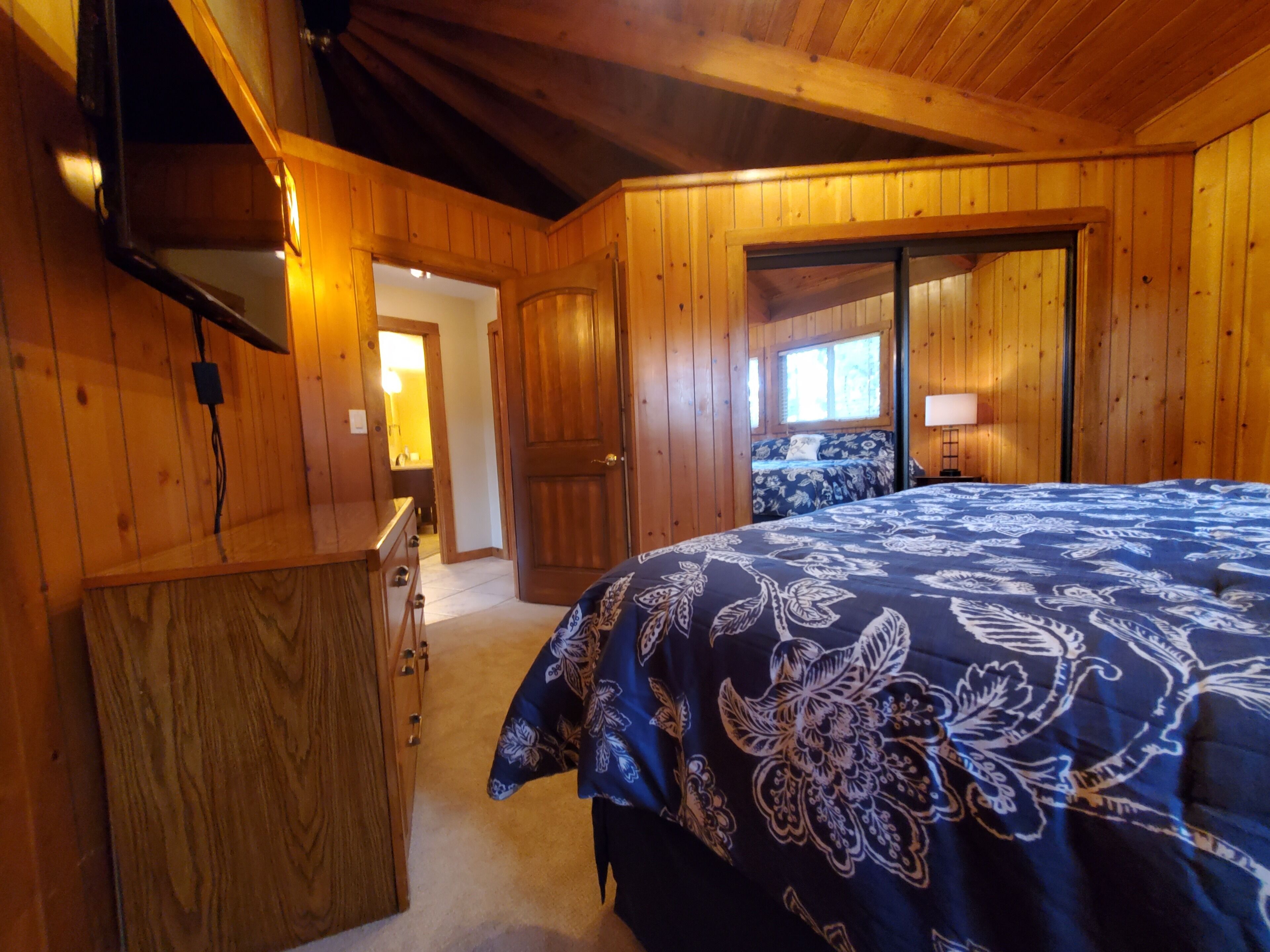 Un dormitorio con paneles de madera, una cama, un aparador y una puerta que da a otra habitación.