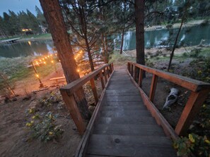 A wooden bridge leading to a dock over a calm lake, surrounded by trees and a grassy area. - Riverfront Cabin - Sunriver/Mt.Bachelor, HotTub, Pet Friendly! (Bend)