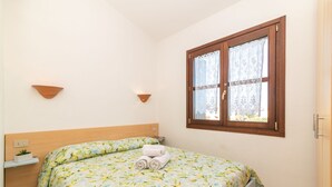Un dormitorio con cama, mesita de noche, ventana con cortinas y lámpara de pared.