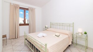 Um quarto com cama, cortinas, janela, mesa de cabeceira com abajur e vista para edifícios.
