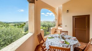 Un balcón con una mesa lista para comer, una puerta y vistas a la vegetación y colinas.