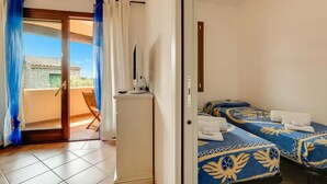 Habitación de hotel con balcón, cama con ropa de cama estampada y un armario blanco.