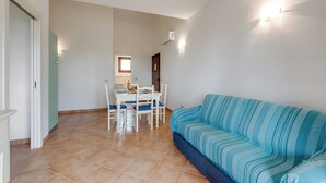 Una sala de estar con un sofá azul a rayas, una mesa de comedor con sillas y una cocina al fondo.