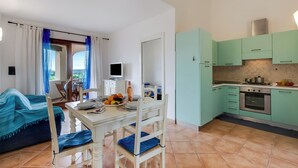 Una cocina compacta con armarios color turquesa, una mesa de comedor blanca y un sofá azul.