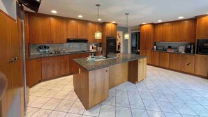 A modern kitchen with wooden cabinets, a central island, and built-in appliances. - The Majestic Retreat Estate (West Lawn)