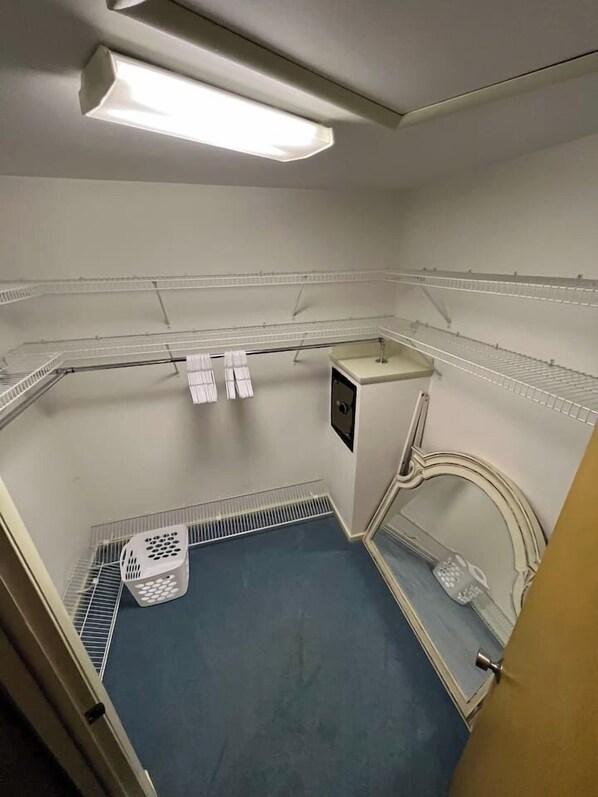Ett litet, avskilt rum med ett blått golv, vita väggar och ett vitt tak. Där finns ett litet handfat, en vit tvättkorg och en vit handdukshängare.