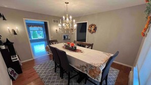 A dining room with a chandelier, a table set with a floral tablecloth, and a view of the outdoors through a doorway. - The Majestic Retreat Estate (West Lawn)