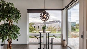 Une pièce moderne dotée d’une grande fenêtre, d’une table ronde avec deux chaises, d’une plante en pot et d’un luminaire suspendu.