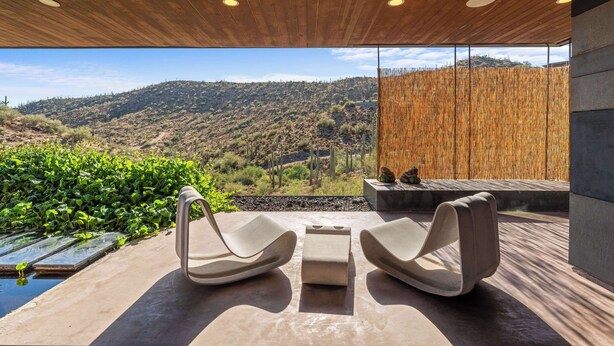 Ein moderner Außenbereich mit zwei Lounge-Stühlen, einem kleinen Tisch und Blick auf eine Berglandschaft.