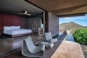 Un dormitorio moderno con una cama grande, un espacio de descanso con sillas y vistas a un paisaje montañoso.