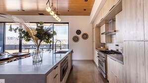 A modern kitchen with a large island, stainless steel appliances, and a view of the desert landscape. - Joshua Tree Hot Tub, Pool, Gym & Fireplace (Yucca Valley)